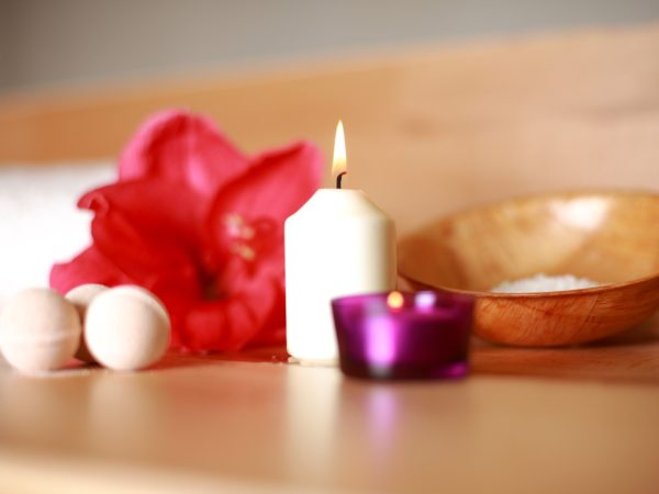 Eine weiße Kerze, eine rote Blüte und zwei Seifenkugeln liegen auf einem Holztisch.